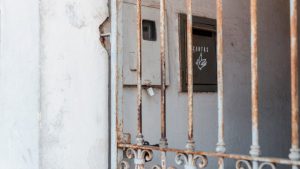 A rusty metal fence frames an old mail drop against a worn wall, creating a rustic atmosphere.
