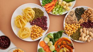 A vibrant mix of legumes, vegetables, nuts, and pasta arranged on white plates showcasing a balanced, healthy diet.